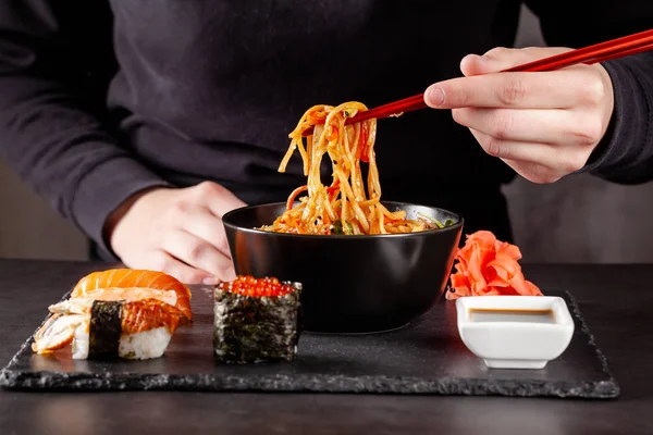 Концепція азіатської кухні. Дівчина Холдинг японський паличками в руці і їдять китайської локшини з чорного плашкового кольору в ресторан. фонове зображення. копія простір — стокове фото