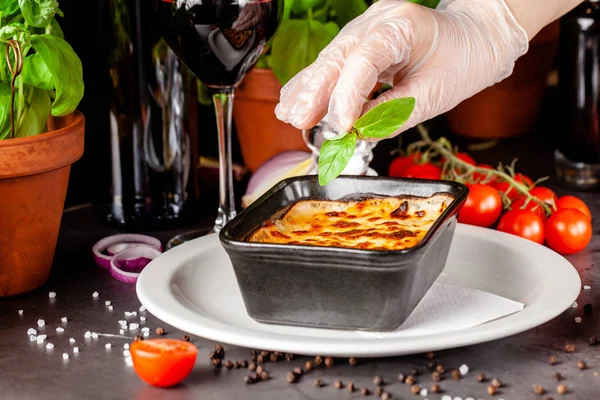 The concept of Italian cuisine. Baked lasagna in a black ceramic baking dish. The chef decorates the dish in the restaurant when serving. Background image. copy space — Stock Photo, Image