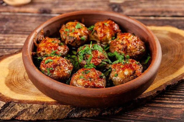 Il concetto di cucina georgiana. Funghi al forno champignons con carne e cilantro. Servire piatti in un ristorante in un piatto di argilla rossa. Su uno sfondo di legno. copia spazio — Foto Stock