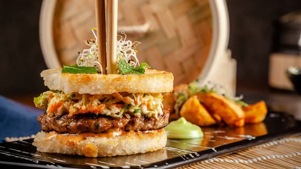 Pan-Asian cuisine concept. Japanese sushi burger made from rice bread, chicken and pork meat patties, lettuce and wasabi sauce. Serving dishes with french fries. copy space — Stock Photo, Image