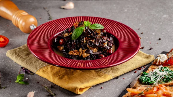 Il concetto di cucina italiana. Papardelle di pasta dolce con noci e canditi. Pasta nera di cacao. Servire piatti in un ristorante in un piatto rosso. copia spazio — Foto Stock