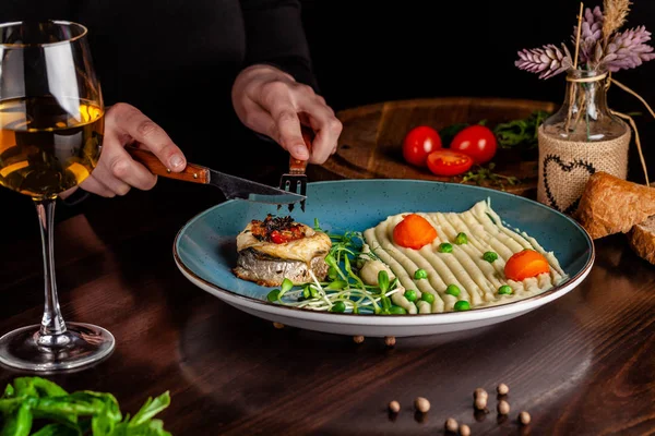Az olasz konyha fogásait. Egy lány egy étteremben rendelkezik villát és egy kést a kezében, és van egy tengeri sügér hal cardato cefre. közelében egy pohár vörösbort. másolási tér — Stock Fotó