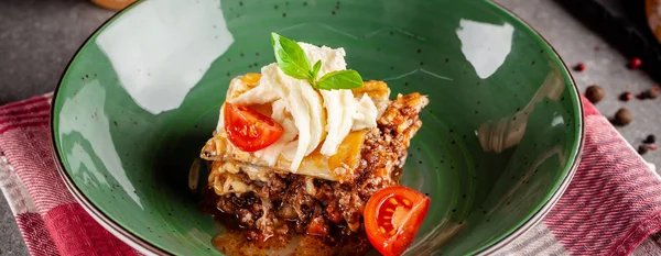 Cucina italiana. Lasagne con carne macinata bolognese. Con suluguni e pomodorini. Servire piatti in un ristorante in un piatto verde. Immagine di sfondo. copia spazio — Foto Stock