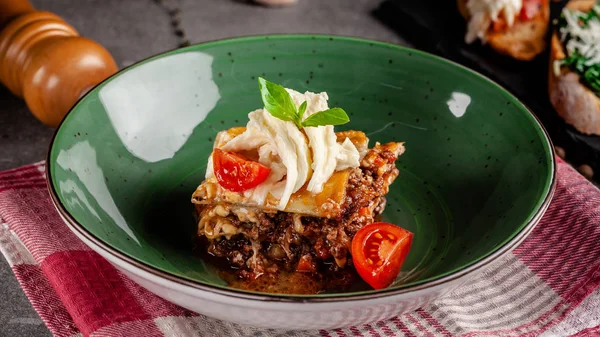 Dania kuchni włoskiej. Lasagna z mięsa mielonego Bolognese. Z serem Ser Suluguni i pomidorami wiśniowym. Posiłki serwowane są w restauracji w zielonej płytce. Obraz tła. miejsce kopiowania — Zdjęcie stockowe