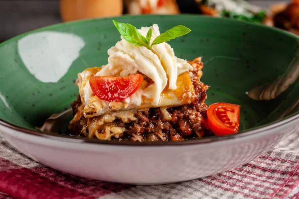 Cucina italiana. Lasagne con carne macinata bolognese. Con suluguni e pomodorini. Servire piatti in un ristorante in un piatto verde. Immagine di sfondo. copia spazio — Foto Stock