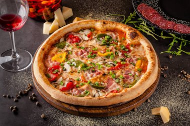 Konsept İtalyan mutfağı. Sebze ve jambon, pastırma ve parmesan peyniri ile gerçek bir pizza. Masadaki malzemeler. Masanın üstündeki bardakta kırmızı şarap. Closeup, arka plan görüntüsü
