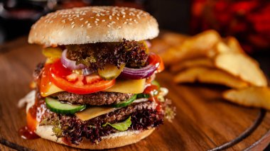 Amerikan mutfağı konsepti. Bir çift domuz eti ve dana eti köfte, domates, salatalık, marul ve peynir ile büyük bir ev yapımı burger. Closeup, arka plan görüntüsü