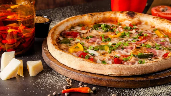 Concept Cuisine italienne. Une vraie pizza aux légumes et jambon, bacon et parmesan. Les ingrédients sur la table. Vin rouge dans un verre sur la table. Gros plan, image de fond — Photo