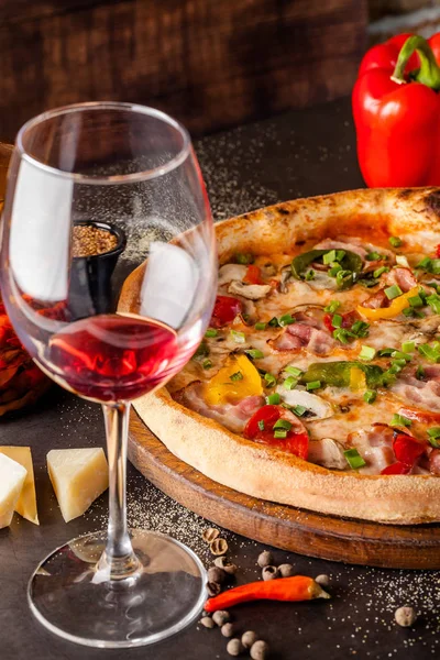 Concept Cuisine italienne. Une vraie pizza aux légumes et jambon, bacon et parmesan. Les ingrédients sur la table. Vin rouge dans un verre sur la table. Gros plan, image de fond — Photo