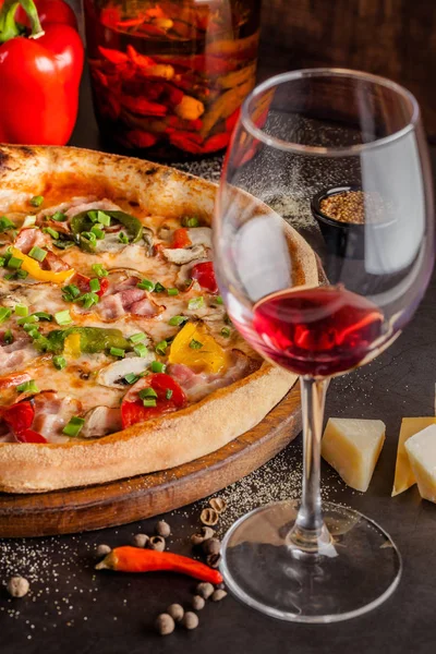 Concept Cuisine italienne. Une vraie pizza aux légumes et jambon, bacon et parmesan. Les ingrédients sur la table. Vin rouge dans un verre sur la table. Gros plan, image de fond — Photo