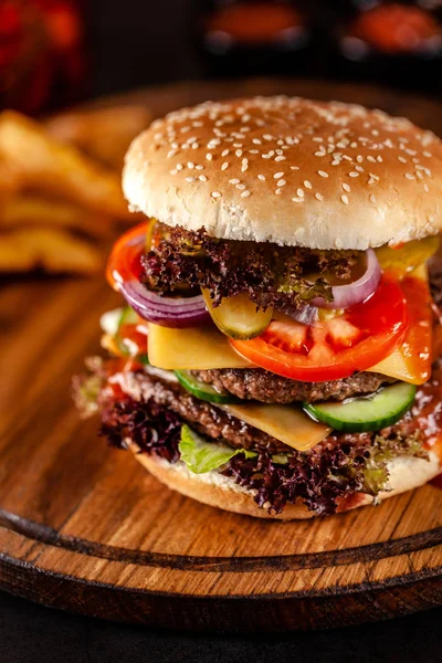 Koncepcja kuchni amerykańskiej. Duży domowy Burger z podwójnym paszteciem wieprzowym i cielęciny, pomidorem, ogórkiem, sałata i serem. Zbliżenie, obraz tła — Zdjęcie stockowe