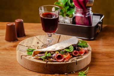 Konsept İtalyan mutfağı. Jambon, domates, mix marul, antep fıstığı, ahşap tahta üzerinde salatalık ile Piadina. Masada bir kadeh kırmızı şarap var. Restoranda güzel servis yemekleri.