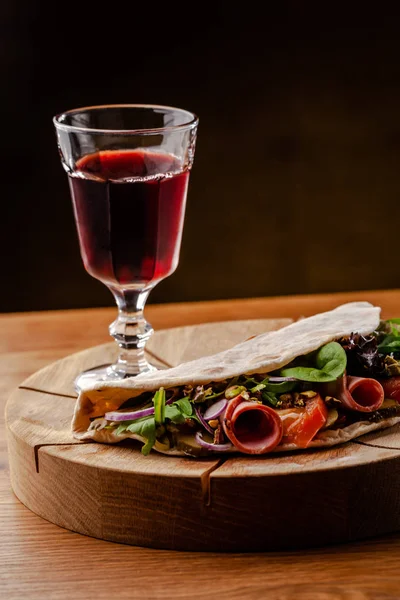 Концепція італійської кухні. Піадіна з шинкою, помідорами, змішати салат, фісташки, огірки на дерев'яній дошці. Келих червоного вина на стіл. Красиві страви в ресторані. — стокове фото