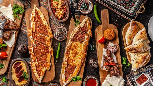 Geleneksel Türk mutfağı. Pizza, pide, pidesi, sucuk, Humus, kebap, Bulgar. Masada birçok yemek var. Restoranda yemekler servis edilir. Arka plan görüntüsü. Üst görünüm, düz yatıyordu