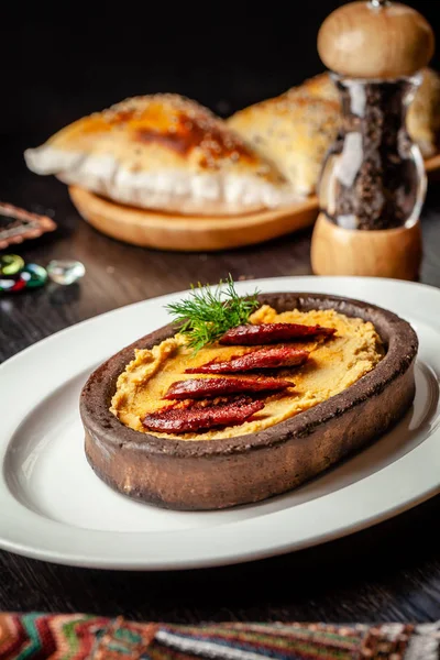 Cuisine traditionnelle turque et arabe. Hummus à la saucisse de salami, dans une assiette d'argile, sur une table en bois. Sur une assiette blanche. Servant des plats au restaurant. espace de copie — Photo