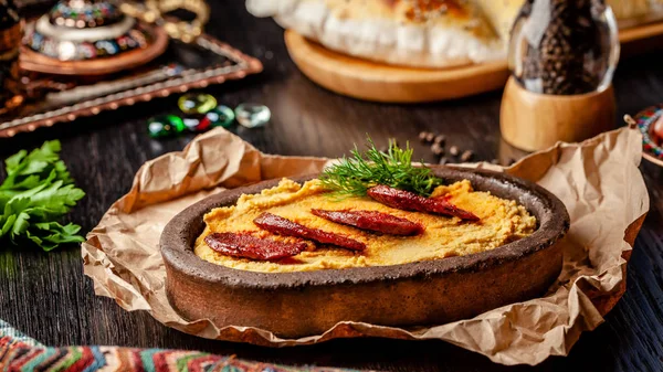 Cuisine traditionnelle turque et arabe. Hummus avec saucisse de salami, dans une assiette d'argile, avec parchemin sur une table en bois. Servant des plats au restaurant. espace de copie — Photo