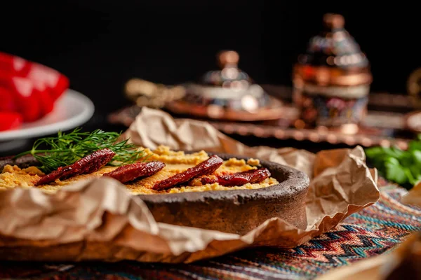 Cuisine traditionnelle turque et arabe. Hummus avec saucisse de salami, dans une assiette d'argile, avec parchemin sur une table en bois. Servant des plats au restaurant. espace de copie — Photo