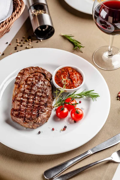 American cuisine. Beef steak with red bbq tomato sauce and cherry tomatoes. A glass of cool wine. Serving dishes on a white plate in a restaurant. Background image. copy space