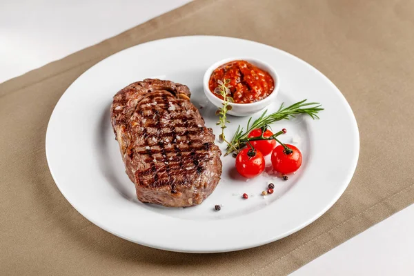 American cuisine. Beef steak with red bbq tomato sauce and cherry tomatoes. A glass of cool wine. Serving dishes on a white plate in a restaurant. Background image. copy space