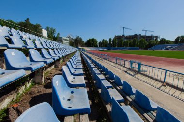 parlak güneşli bir günde mavi gök mavisi oturma Stadyumu yeşil çimen alanındaki temizleyin ve arka plan binada çalışan vinçler izlemek
