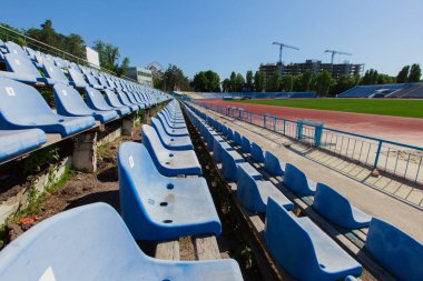 parlak güneşli bir günde mavi gök mavisi oturma Stadyumu yeşil çimen alanındaki temizleyin ve arka plan binada çalışan vinçler izlemek