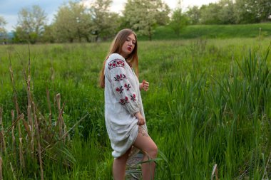 Nakış seductively yeşil bahar çayır üzerinde poz ile keten uzun gömlekli Ukraynalı kız