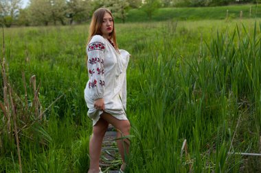 Nakış seductively yeşil bahar çayır üzerinde poz ile keten uzun gömlekli Ukraynalı kız