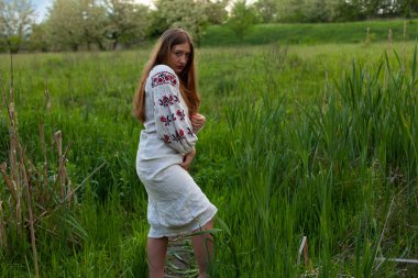 Nakış seductively yeşil bahar çayır üzerinde poz ile keten uzun gömlekli Ukraynalı kız