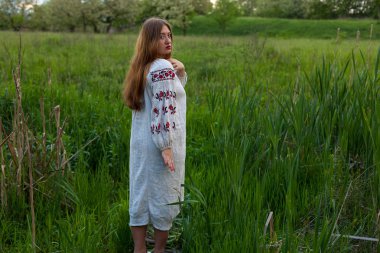 Nakış seductively yeşil bahar çayır üzerinde poz ile keten uzun gömlekli Ukraynalı kız