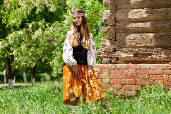 Beautiful slender Ukrainian woman in embroidery on the background of a wooden frame of a barn in the village