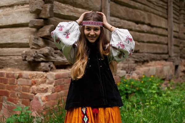 Beautiful slender Ukrainian woman in embroidery on the background of a wooden frame of a barn in the village