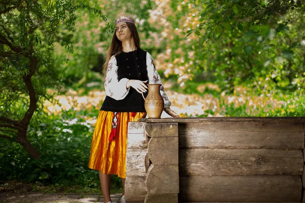 Beautiful Ukrainian woman is wearing embroidery near a wooden well