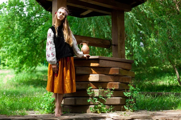 Beautiful Ukrainian woman is wearing embroidery near a wooden well