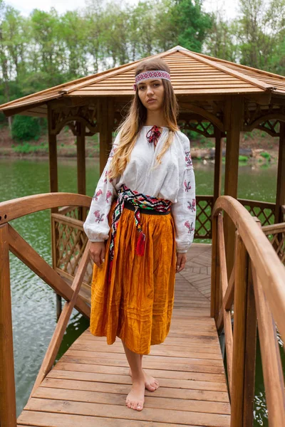 Beautiful Ukrainian woman dressed in embroidery in a wooden summer altanka on a lake