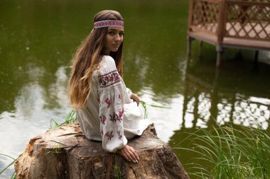 Nakış içinde giymiş Ukraynalı kadın çok güzel bir güdük bir göl kıyısında oturur