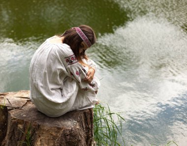 Nakış içinde giymiş Ukraynalı kadın çok güzel bir güdük bir göl kıyısında oturur