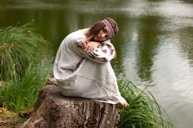 Nakış içinde giymiş Ukraynalı kadın çok güzel bir güdük bir göl kıyısında oturur