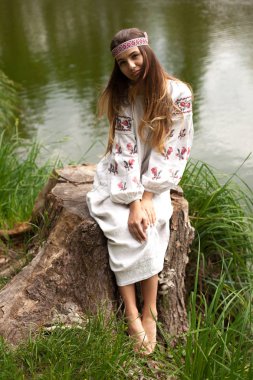 Nakış içinde giymiş Ukraynalı kadın çok güzel bir güdük bir göl kıyısında oturur