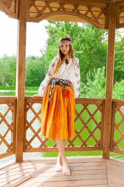 湖畔に木製の夏 Altanka の刺繍に身を包んだ美しいウクライナの女性 — ストック写真