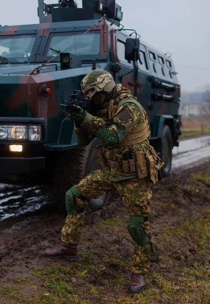 a soldier moves undercover with an armored car on the side of a road in the rain