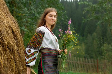 Bir buket kır çiçeğiyle dağınık saçlı kız samanlığın yanında duruyor.