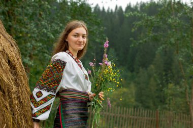 Bir buket kır çiçeğiyle dağınık saçlı kız samanlığın yanında duruyor.