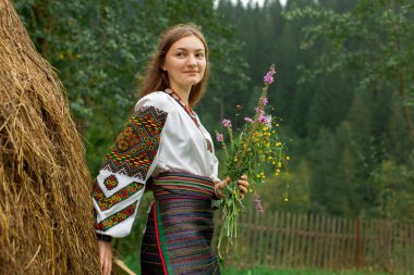 Bir buket kır çiçeğiyle dağınık saçlı kız samanlığın yanında duruyor.