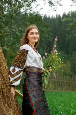 Bir buket kır çiçeğiyle dağınık saçlı kız samanlığın yanında duruyor.