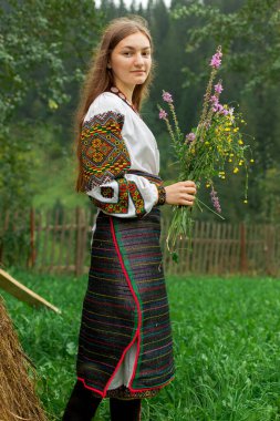 Bir buket kır çiçeğiyle dağınık saçlı kız samanlığın yanında duruyor.