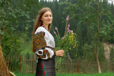 Bir buket kır çiçeğiyle dağınık saçlı kız samanlığın yanında duruyor.