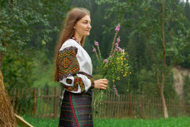 Bir buket kır çiçeğiyle dağınık saçlı kız samanlığın yanında duruyor.