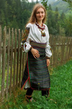 Bir buket kır çiçeğiyle gevşek saçlı kız tahta bir çitin önünde duruyor.