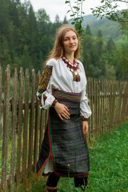 Bir buket kır çiçeğiyle gevşek saçlı kız tahta bir çitin önünde duruyor.