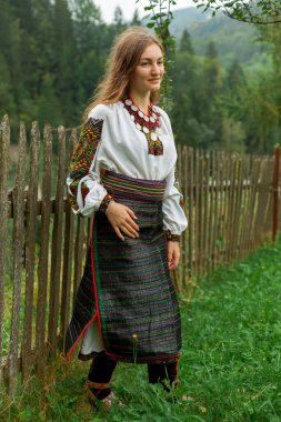 Bir buket kır çiçeğiyle gevşek saçlı kız tahta bir çitin önünde duruyor.